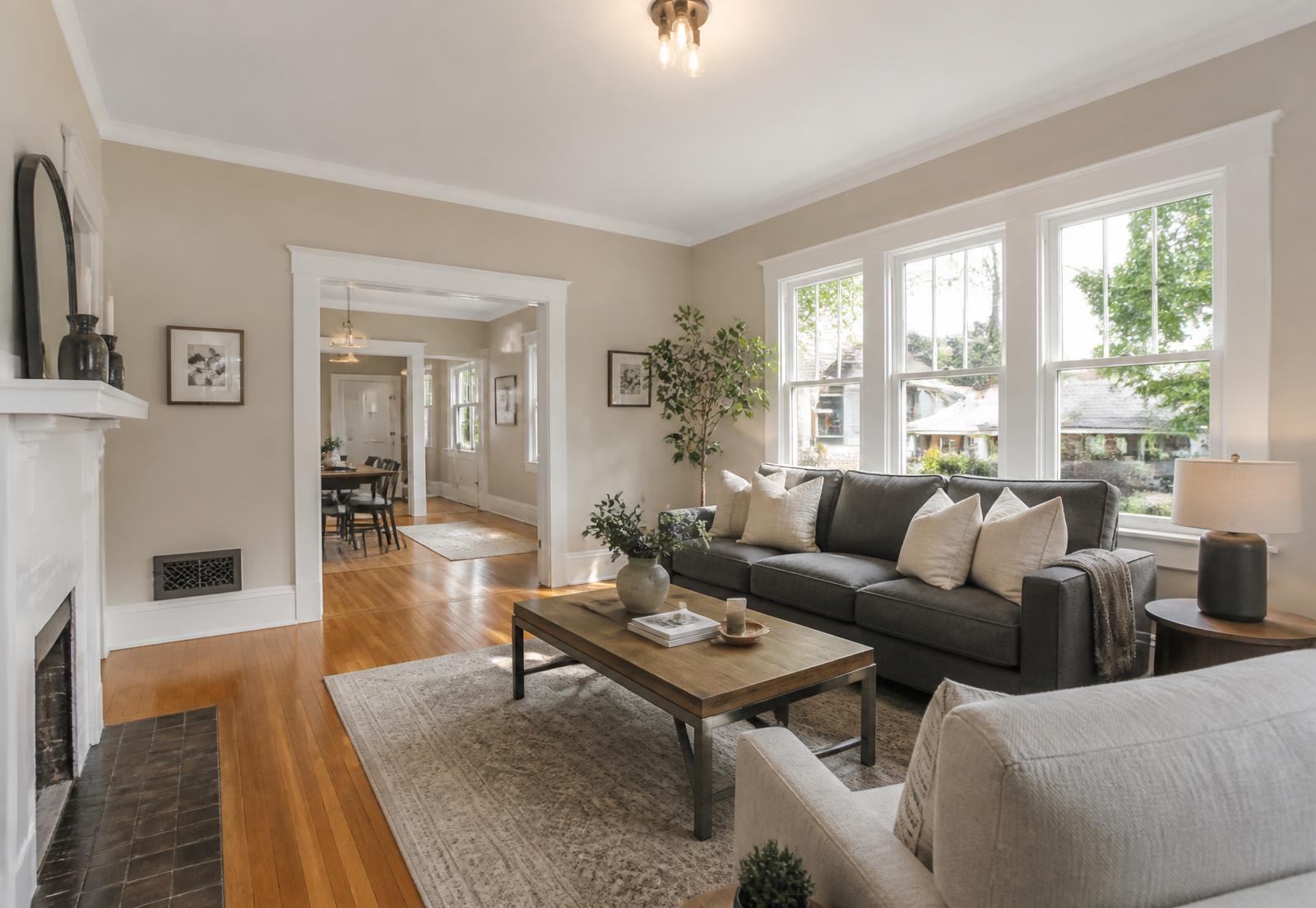 Renovated living room with a white fireplace, hardwood floors and tall windows